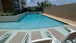 A swimming pool with lounge chairs and a building in the background. - Walk to Palm Beach • Pool • Modern 2BR Aruba Condo (Noord)