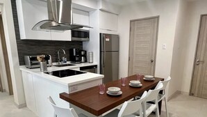 A modern kitchen with white cabinetry, a built-in stove, and a dining area with white chairs and a wooden table. - Walk to Palm Beach • Pool • Modern 2BR Aruba Condo (Noord)