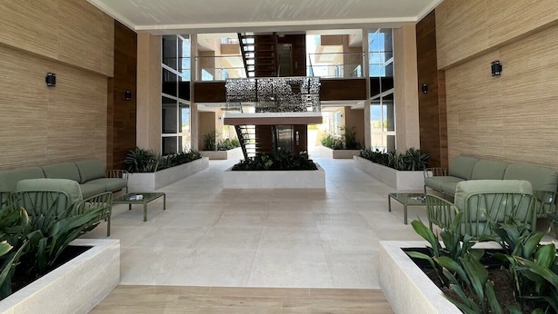 A spacious lobby with a high ceiling, modern furniture, and a central decorative structure. - Walk to Palm Beach • Pool • Modern 2BR Aruba Condo (Noord)