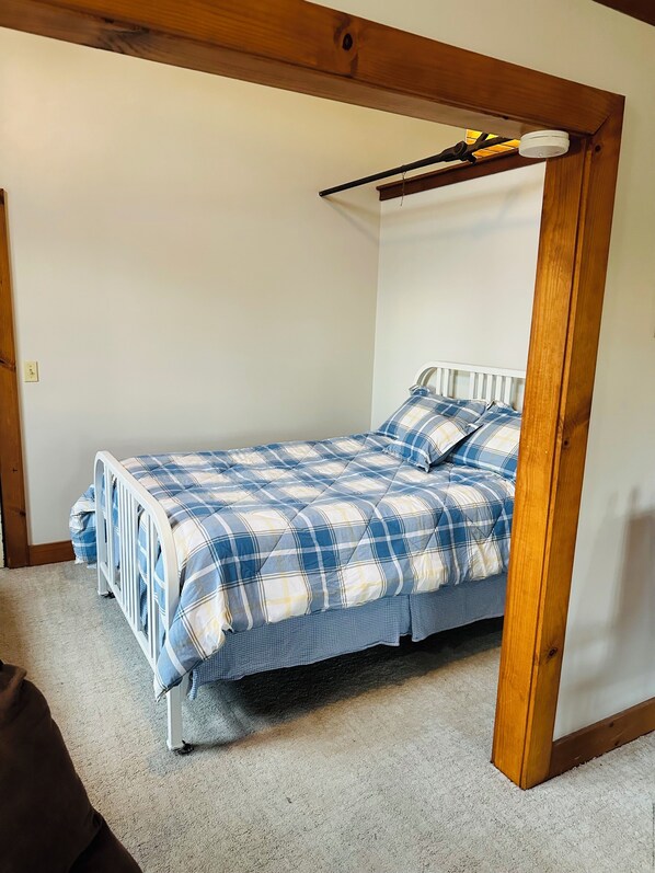 Un lit simple avec une couette à carreaux bleus et blancs, dans une pièce dont le plafond est orné de poutres en bois.