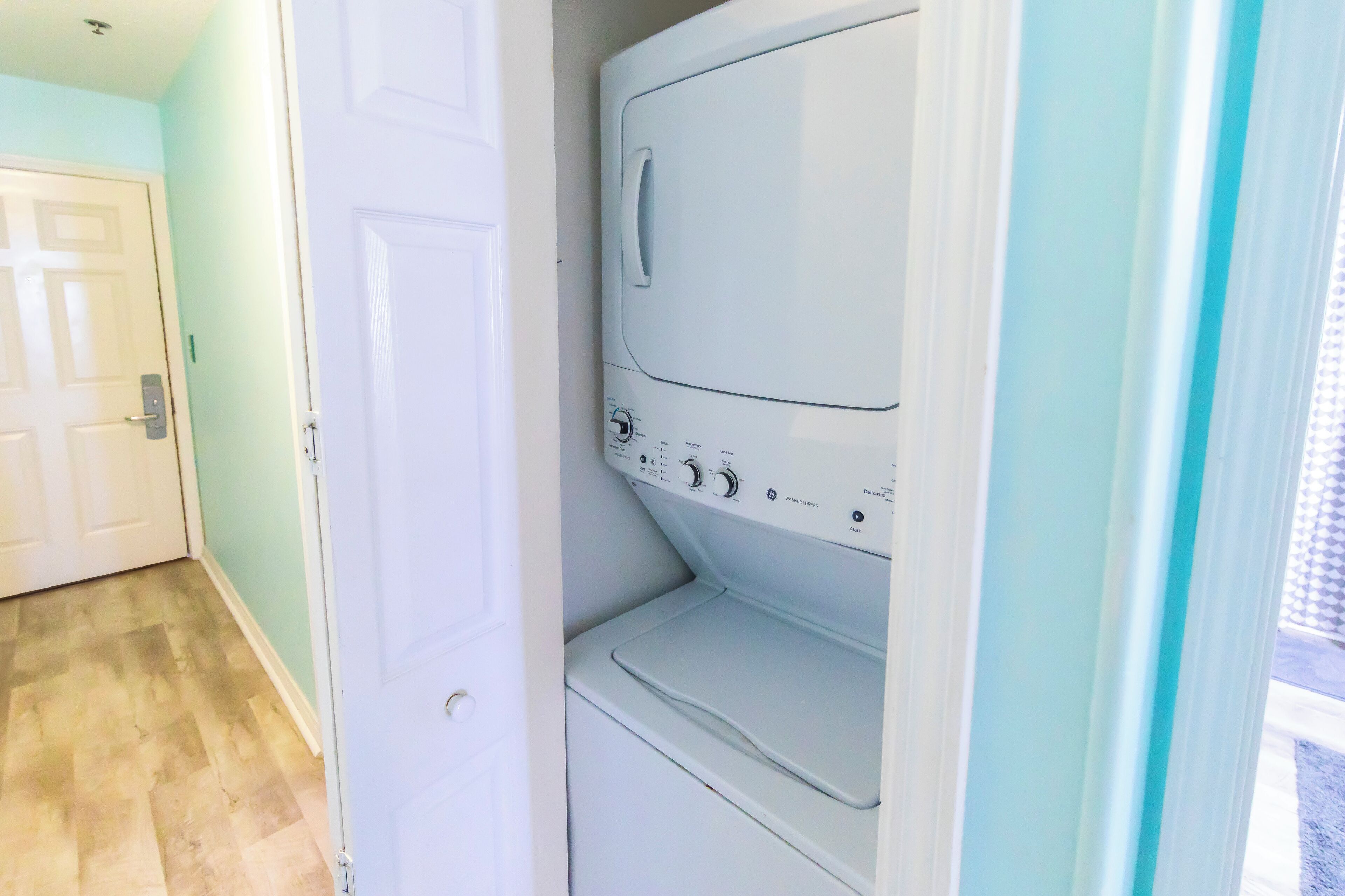 A laundry room with a front-loading washer and dryer, a wooden floor, and a white door.