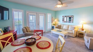 A living room with a white table, red and beige chairs, a beige sofa, and a white coffee table. There are two windows with blinds, a ceiling fan, and a lamp on a side table. - Gulf View, Community Pool, Tennis, Beach Access (Santa Rosa Beach)