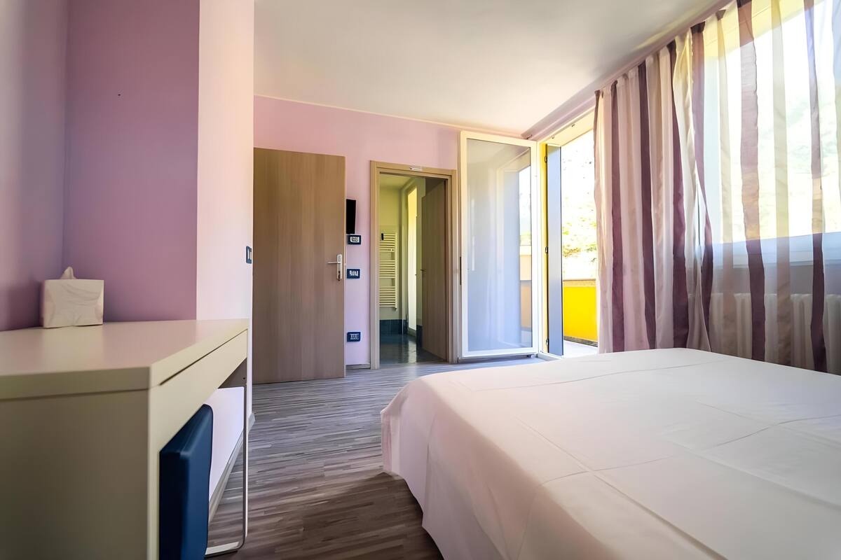 Ein Hotelzimmer mit Bett, Schreibtisch und einer Tür, die auf einen Balkon führt.