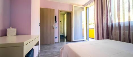 A hotel room with a bed, a desk, and a door leading to a balcony.