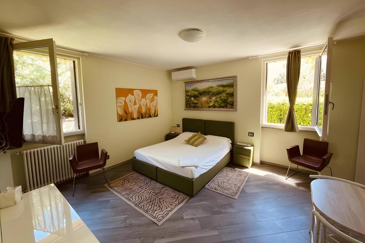 Ein Schlafzimmer mit einem Bett, zwei Stühlen, einem Schreibtisch und Kunstwerken an den Wänden.