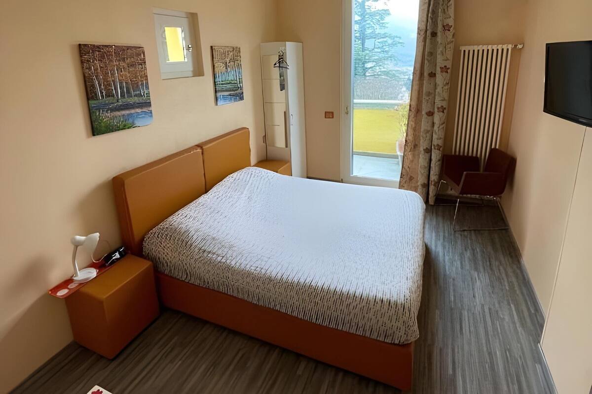 Ein Schlafzimmer mit Bett, Nachttisch, Kleiderschrank, Fernseher und Blick ins Freie.