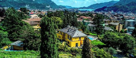 A yellow building surrounded by greenery, with a mountainous backdrop and a lake in the distance.
