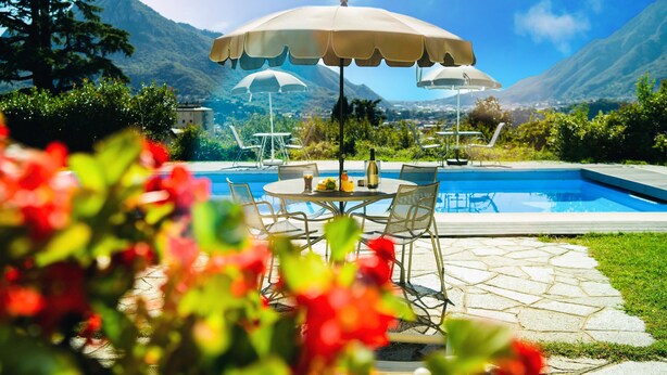 A pool area with outdoor seating and umbrellas, surrounded by greenery and mountains. - Montebello Lake (Lecco)