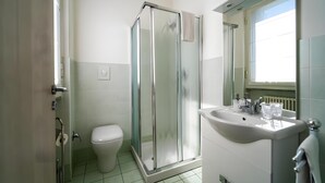 A modern bathroom with a glass-enclosed shower, a toilet, and a sink with a mirror. - Montebello Lake (Lecco)