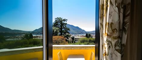 A balcony with a yellow wall, a white table, and two wicker chairs.