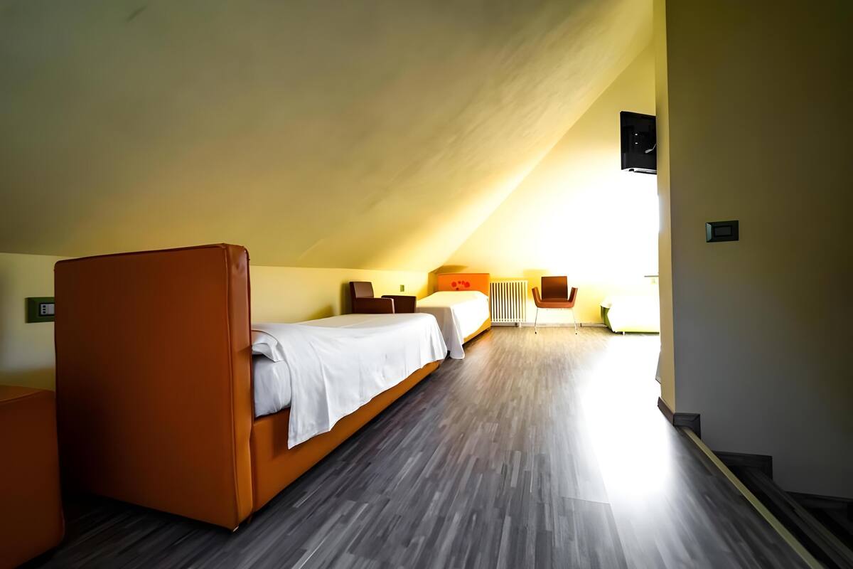Ein Zimmer mit schrägem Dach, zwei Betten mit weißen Laken, ein kleiner Tisch und ein Stuhl.