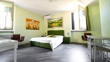 Habitación de hotel con cama, una mesa, dos sillas, radiador y obras de arte en las paredes.