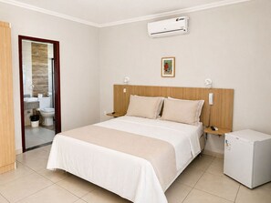 A hotel room with a bed, bedside tables, an air conditioner, a refrigerator, and a bathroom visible through an open door.