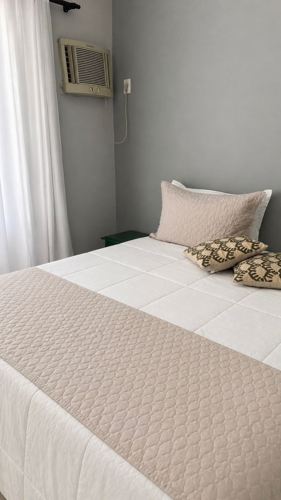 A bed with a quilted bedspread, a pillow with a leaf pattern, and a wall-mounted air conditioner.