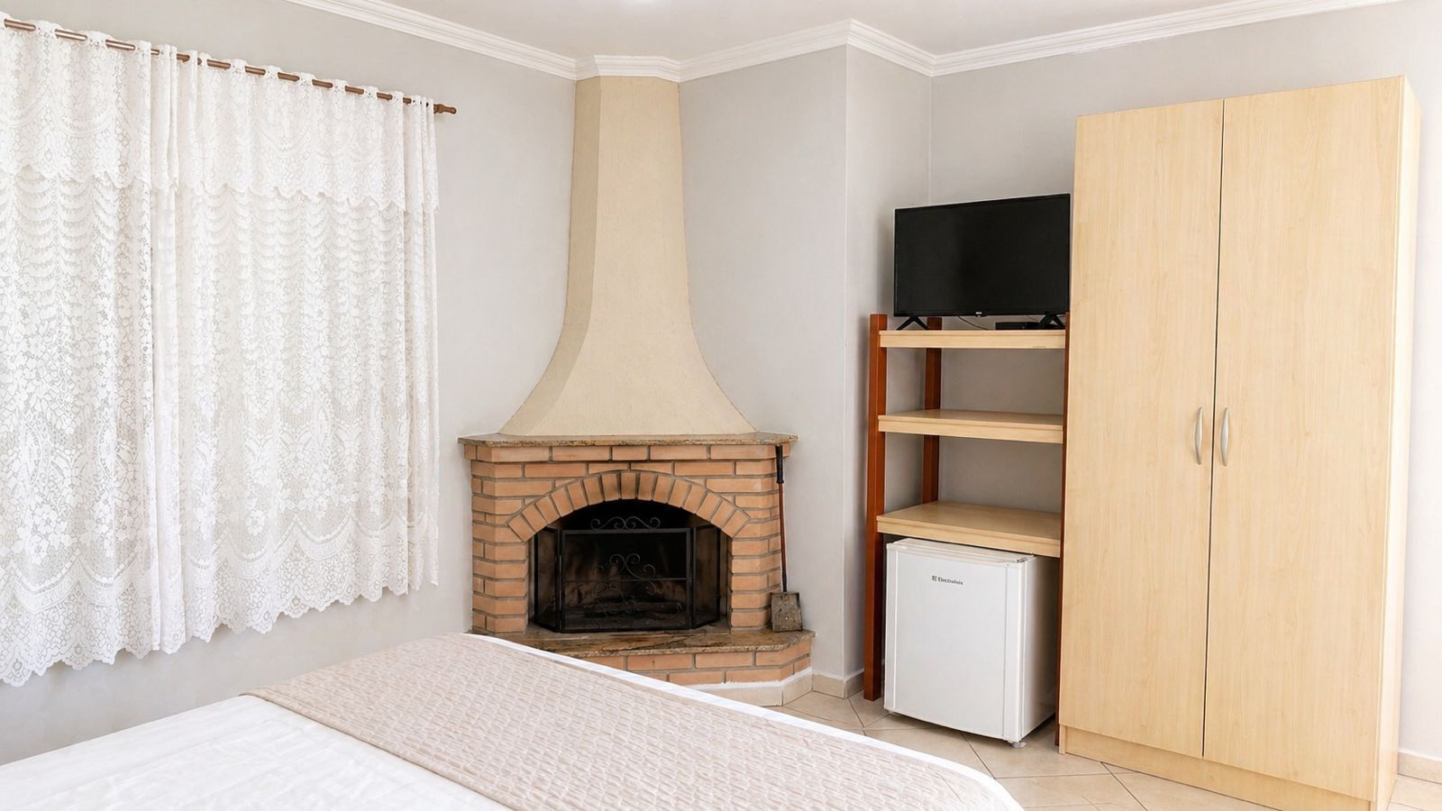 Une chambre avec une cheminée en briques, un téléviseur posé sur une étagère, une armoire et un lit.