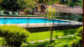 Una piscina rodeada de abundante vegetación y un pequeño edificio con techo rojo.