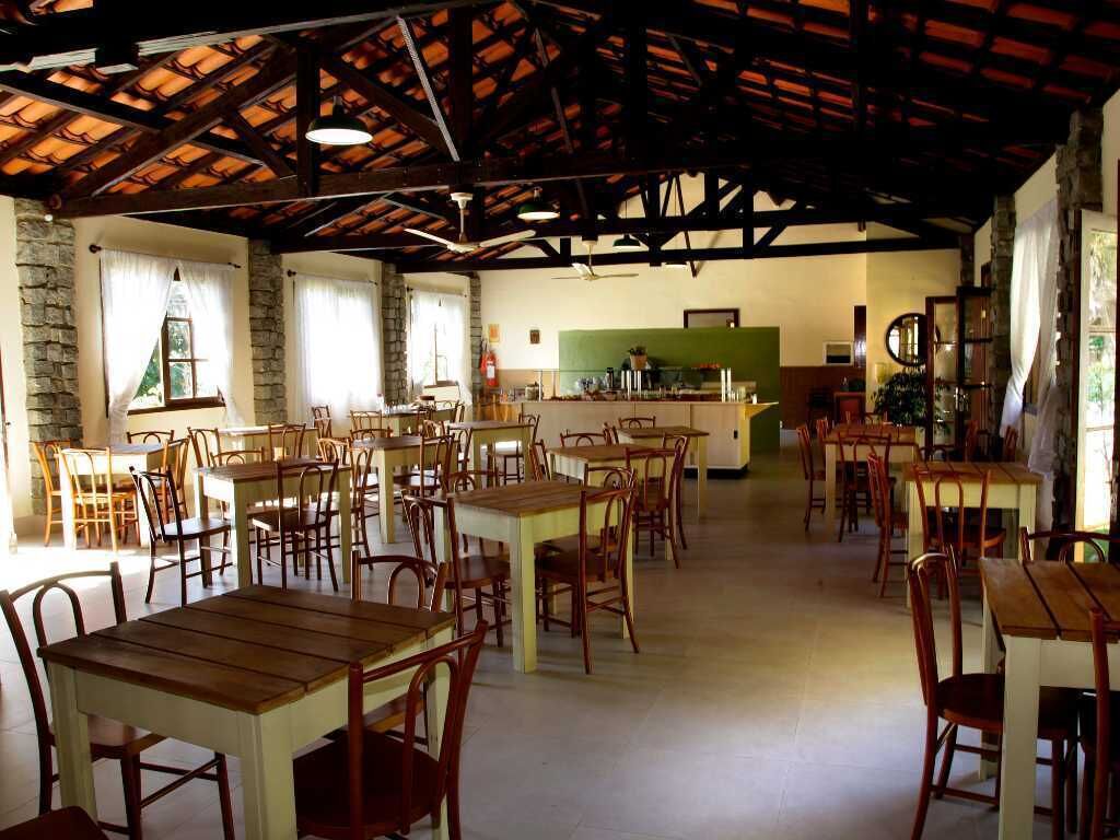 A spacious dining area with wooden tables and chairs, a kitchen in the background, and a stone wall on one side.