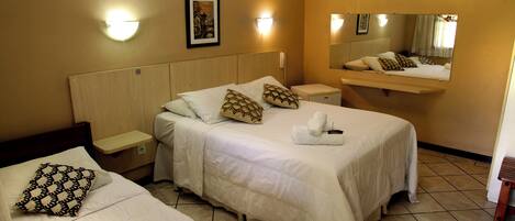 A hotel room with two beds, a bedside table, a nightstand, a wall-mounted mirror, and a wall-mounted light fixture.