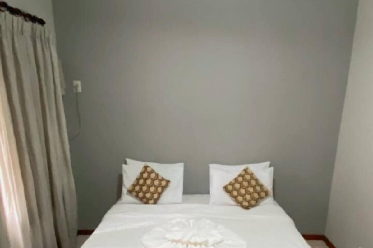Ein Schlafzimmer mit einem Bett, weißer Bettwäsche, einer orangefarbenen Tagesdecke und zwei Zierkissen.