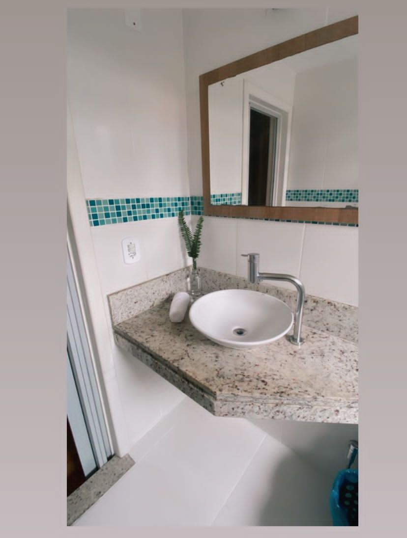 Un baño con lavamanos blanco, un espejo y una planta verde.