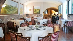 Ein Restaurant mit runden Tischen, gestreiften Stühlen, großen Fenstern und Bildern an den Wänden.