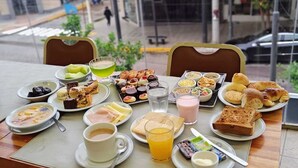 Mesa posta com diversos itens de café da manhã, incluindo doces, frutas e bebidas.