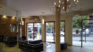 Um saguão de hotel com balcão de recepção, área de estar e grandes portas de vidro que dão para o exterior.