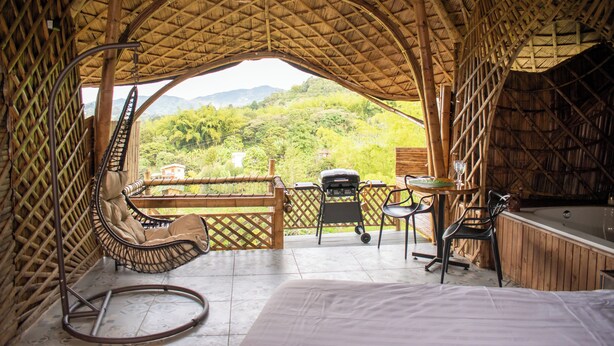 Un espacio al aire libre con techo de paja, jacuzzi, asientos y vistas a las montañas.