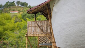 Estructura de bambú adosada a un edificio blanco, con vistas a una colina y vegetación en el fondo.