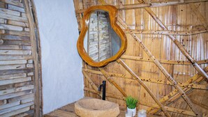 Un baño rústico con pared de madera, lavamanos de piedra, espejo con marco de madera y una pequeña planta en maceta.
