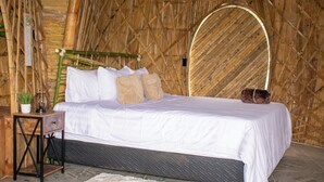 Una cama con ropa blanca, una mesita de noche con una planta y una almohada decorativa.