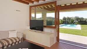 A living room with a TV on a cabinet, a sofa, and a view of a swimming pool.
