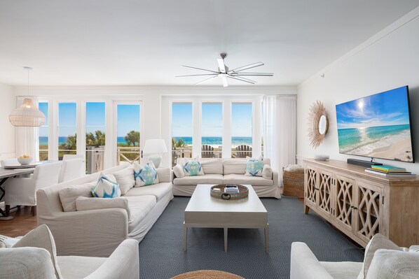 A spacious living room with a large window overlooking the ocean, a ceiling fan, and a flat-screen TV on a wooden cabinet. - Gulf Front, Resort Amenities, Incredible Views and Balconies (Inlet Beach)