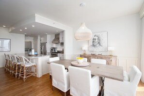 A modern kitchen with white cabinetry, a central island, and a dining area with white chairs and a wooden table. - Gulf Front, Resort Amenities, Incredible Views and Balconies (Inlet Beach)