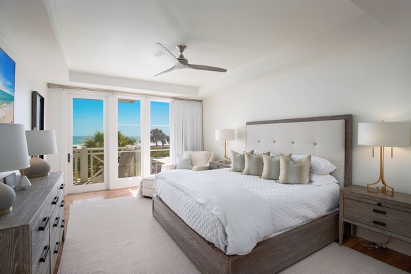 Une chambre spacieuse avec un grand lit, un ventilateur de plafond et une vue sur l’extérieur grâce à une porte-fenêtre coulissante.