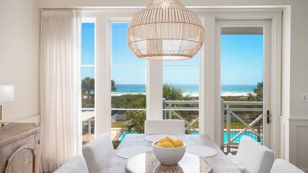 A dining area with a view of the ocean, a pool, and a white table with a bowl of fruit. - Golf Cart, 30A Watersound Gated Community, Beach Views, Gulf Front, Large Pool (Inlet Beach)