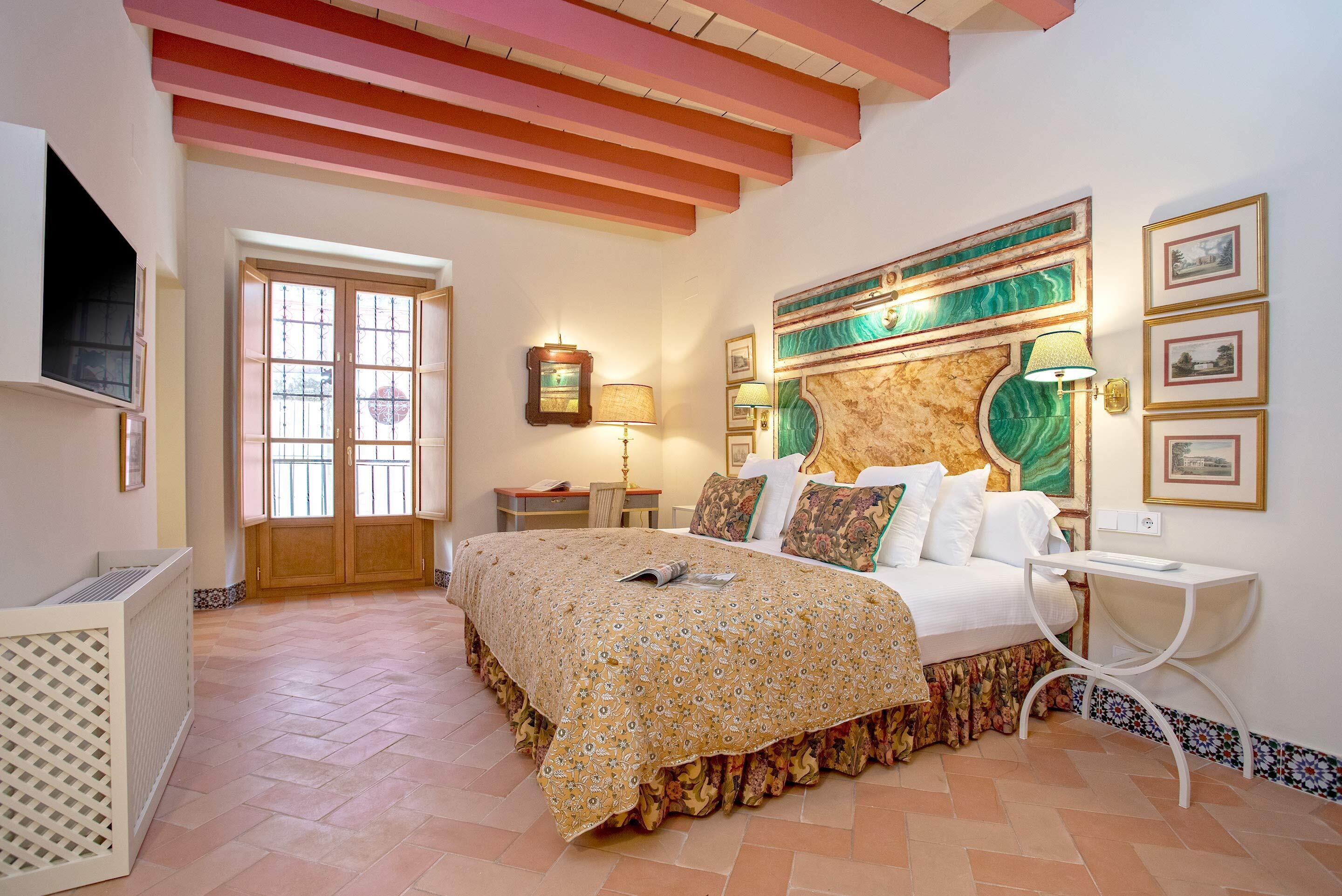 A bedroom with a bed, a television, a door, and a wall with framed pictures.