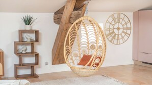 A room with a hanging rattan chair, a wooden shelf with decorative items, and a large wall clock. - Le 1789, Gîte Haut de Gamme Pour les Amoureux de Rêverie, Avec Piscine et Sauna (Pézenas)