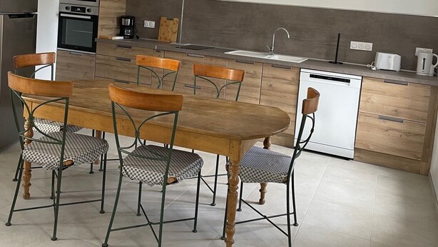 A modern kitchen with a dining area, featuring a central island, wooden cabinets, and a built-in oven.