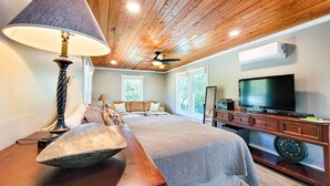 A bedroom with a wooden ceiling, a bed, a television, and a desk with a lamp. - Beachcomber – Small Space, Big Paradise! (Topsail Beach)