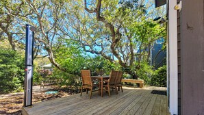 A wooden deck with a table and chairs, surrounded by trees and a house. - Beachcomber – Small Space, Big Paradise! (Topsail Beach)