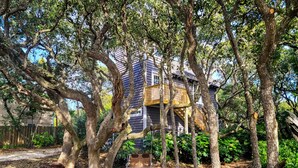 A house surrounded by large trees with a wooden deck and a swing. - Beachcomber – Small Space, Big Paradise! (Topsail Beach)