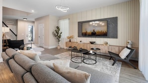 A modern living room with a large flat-screen TV mounted on the wall, a grey sectional sofa, a coffee table, and a side table. - Reunion Retreat 4-Bedroom Home w/ Playful Touches (Kissimmee)