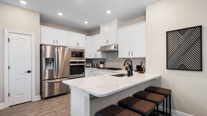 A modern kitchen with white cabinets, stainless steel appliances, and a central island with bar stools. - Reunion Retreat 4-Bedroom Home w/ Playful Touches (Kissimmee)