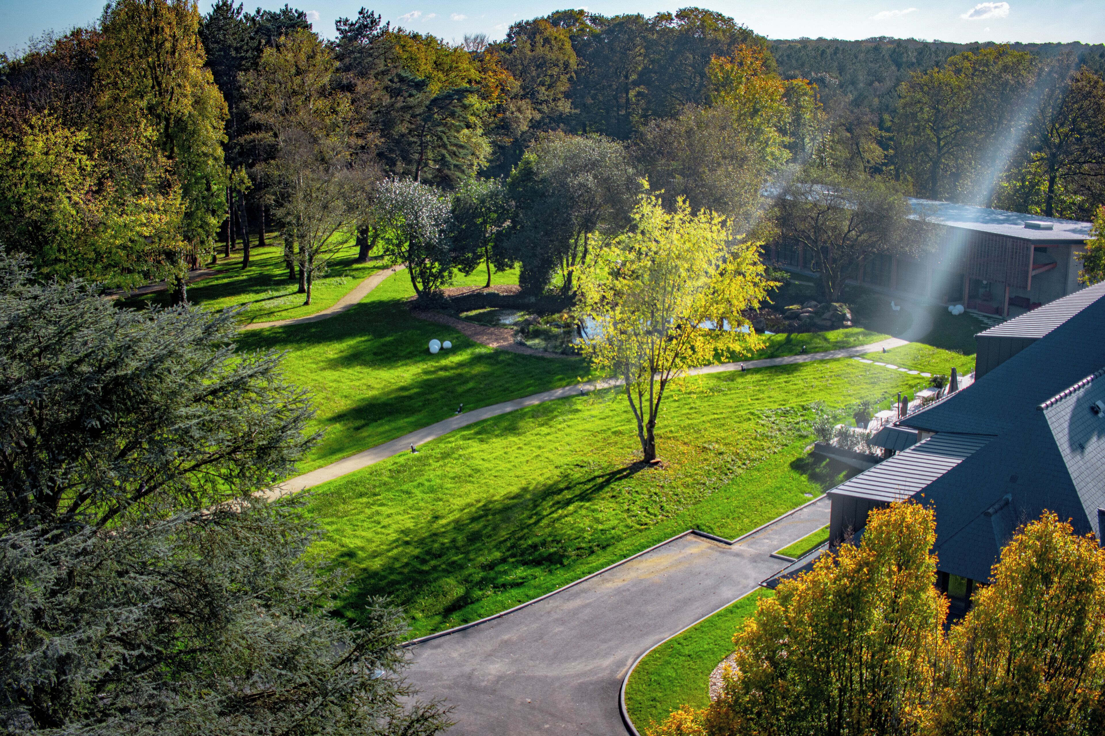 A park with a curved pathway, a building with a sloped roof, and a body of water in the background.