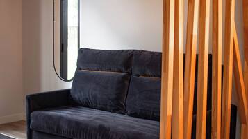 Et moderne værelse med en mørkegrå sofa, en træskærm og et spejl på væggen.