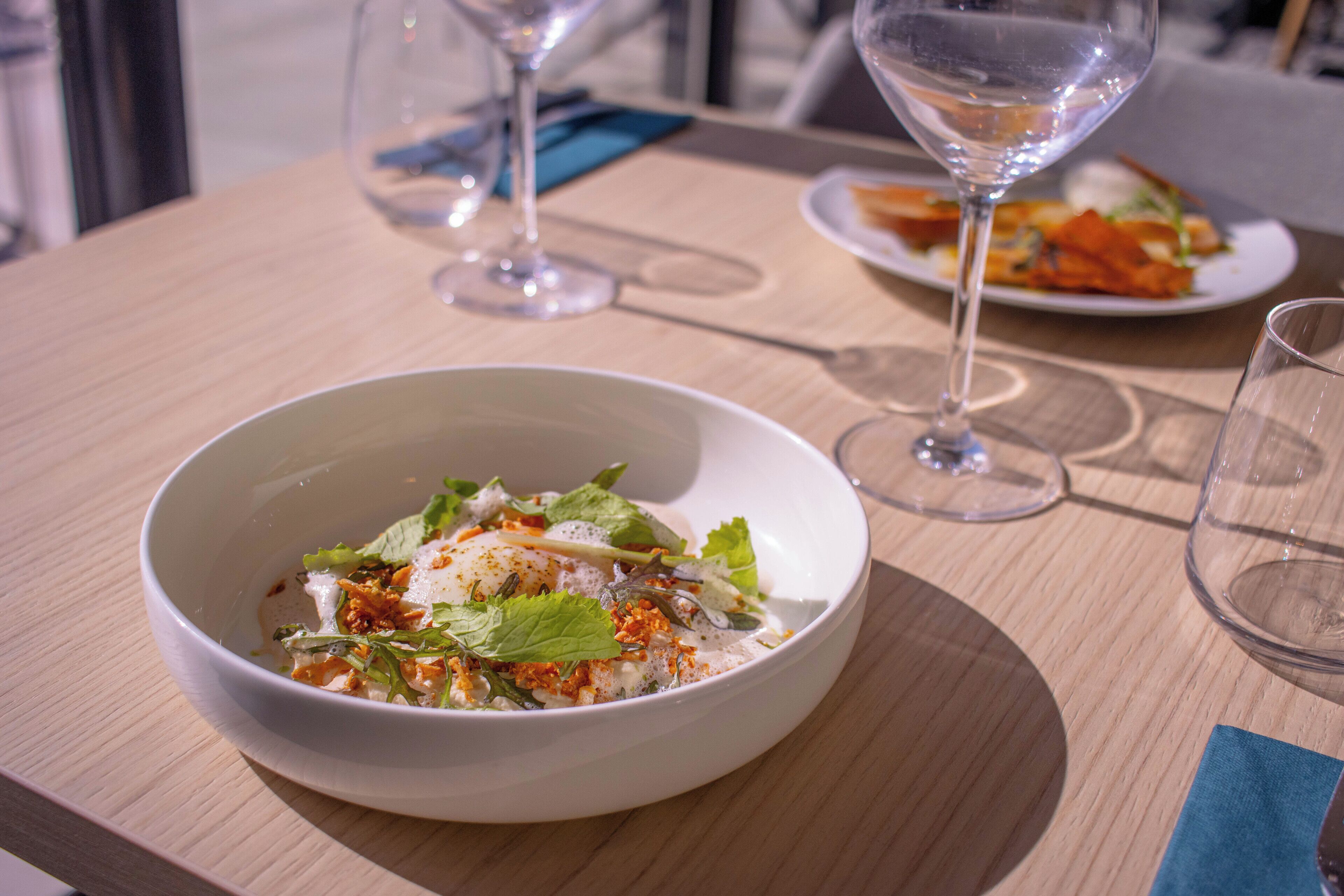 Une table à manger avec un saladier rempli de salade, un verre à vin et une assiette de nourriture.