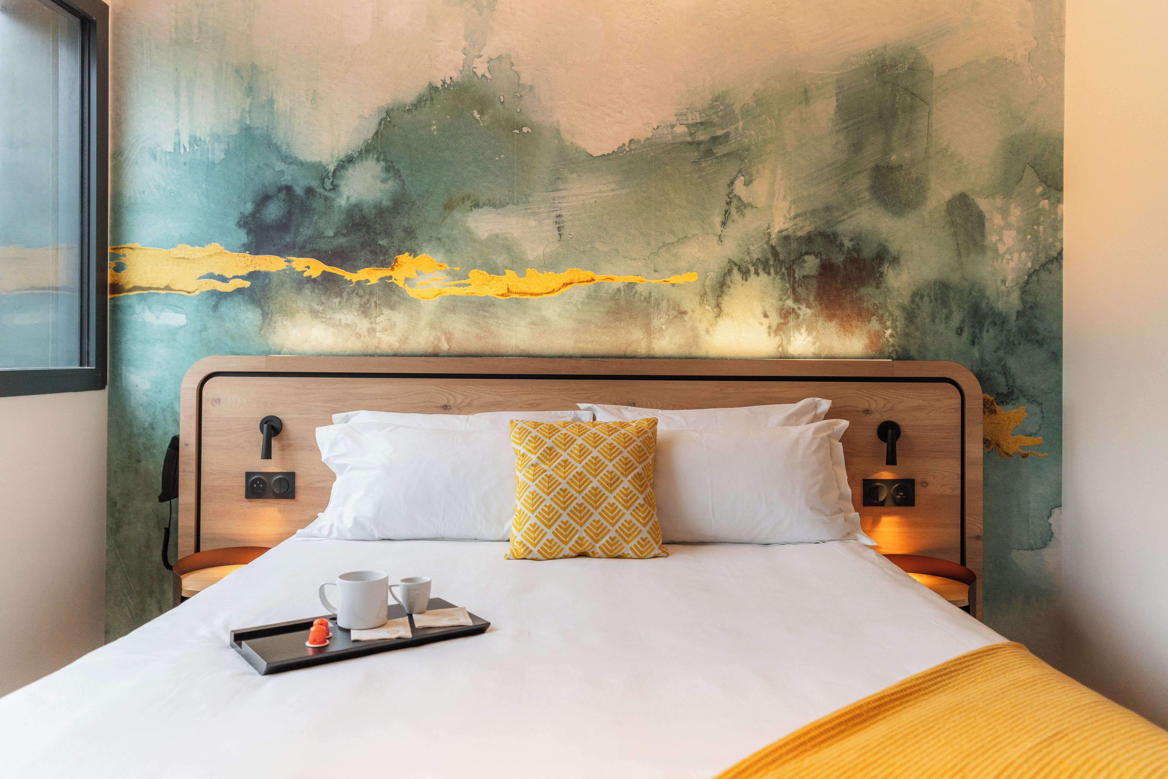 A hotel room with a bed, a tray with a cup and a small orange object, and a wall with a textured abstract design.