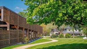 Un edificio moderno con una galería techada, un césped cuidado y un gran árbol que da sombra.
