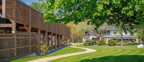 A modern building with a covered walkway, a well-maintained lawn, and a large tree providing shade.